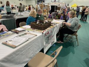 A woman sits at an Ask a Master Gardener table.